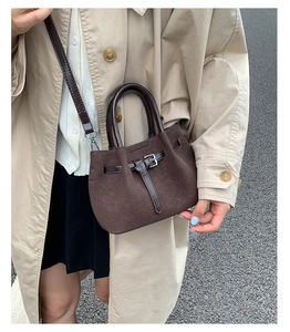 Close-up detail of stylish brown bucket crossbody handbag with stylish belt buckle design.