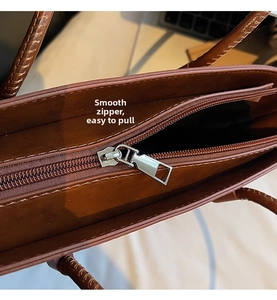 Detail view of smooth metal zipper and woven handle on vintage brown leather tote bag