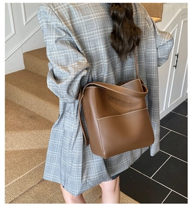 Détail du sac seau marron avec coutures contrastées sur un mannequin en blazer gris