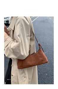 Outdoor shot of a brown suede baguette shoulder bag with elegant vertical stitching detail
