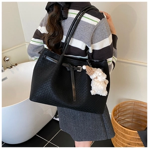 Détail du sac cabas tressé noir avec boucles et breloque en forme d'ours en peluche blanc