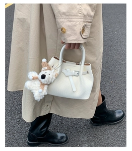 Detail shot of stylish white woven handbag with cute bear pendant and chic belt buckle design.