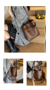 Detail of a brown leather bucket bag with contrast white stitching and wide shoulder strap