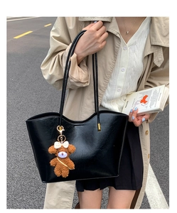 Détail d'un sac cabas en cuir noir brillant avec breloque d'ours et trench-coat beige