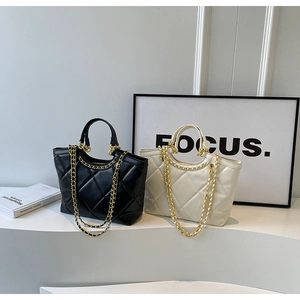 Quilted tote bags in black and beige with gold chain straps shown in a modern interior