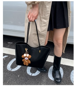 Vue lifestyle de rue d'un grand sac cabas noir avec un adorable charm en forme d'ours