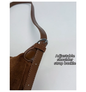 Detail of adjustable shoulder strap with silver metal buckle on a brown suede handbag