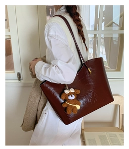 Détail d'un grand sac cabas marron foncé brillant avec un pendentif ours en peluche
