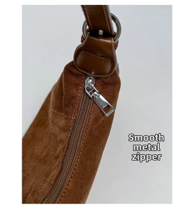 Close-up of smooth silver metal zipper and brown suede texture on a crossbody bag