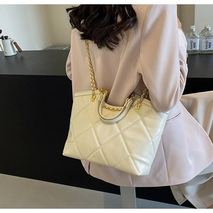 Detail of quilted creamy white tote bag featuring gold chain strap and diamond stitch texture