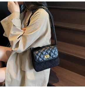 Detail of black quilted crossbody bag with gold twist lock on a beige trench coat