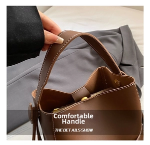 Detail of dark brown leather bucket bag with white contrast stitching and gold zipper