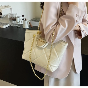 Quilted cream tote bag with gold chain strap shown in a modern coffee shop setting