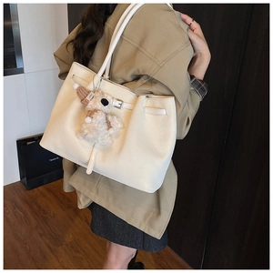 Détail du sac cabas tissé crème avec boucle en cuir et un joli porte-clés en peluche