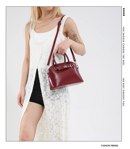 Detail of burgundy glossy patent leather shell bag with round handles and silver hardware