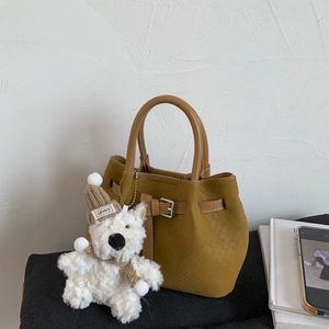 Detail of mustard yellow woven bucket bag with a cute plush bear charm and metal buckle