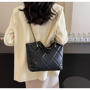 Rear view of a model wearing the large black quilted tote bag with chain strap