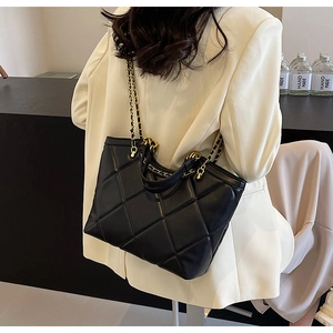 Close-up of quilted black tote bag with gold chain strap on model in white blazer