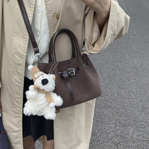 Detail of a brown suede bucket bag with leather buckle and cute plush bear charm