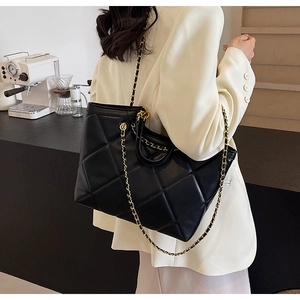 Detail of black quilted tote bag featuring gold chain strap and sleek leather texture