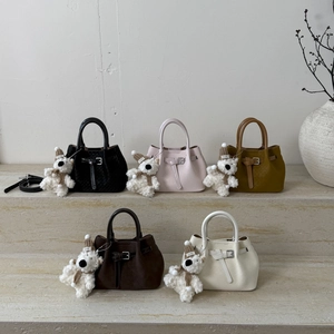Textured bucket bags in five colors with cute bear charms on stone steps display