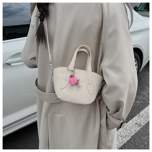 Chic beige mini trapezoid crossbody bag with heart pendant shown on shoulder