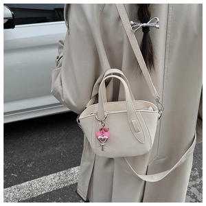 Close-up of cream mini handbag with pink heart pendant and silver key charm
