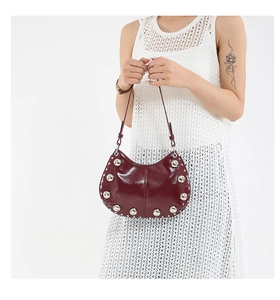 Close-up of deep burgundy crescent bag featuring glossy leather and silver rivet details