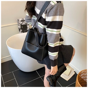 Detail view of black leather bucket bag with contrasting white stitching and slim strap
