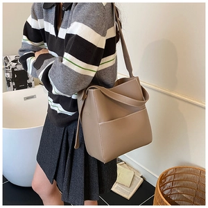 Detail view of coffee leather bucket bag featuring white contrast stitching and wide strap