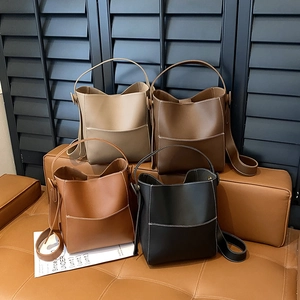 Minimalist leather bucket bags with contrast stitching in four colors on a leather bench