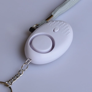 Detailed close-up of white egg-shaped personal security alarm with lanyard and metal keychain
