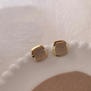 Orecchini a perno quadrati in oro opaco in un piatto di ceramica bianca, stile retrò