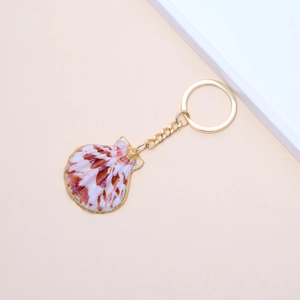 Detail of natural seashell keychain with gold plated edges and golden metal key ring