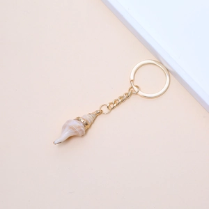Detail of natural spiral conch keychain with gold metal ring and polished shell texture