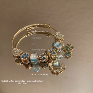 Detail of gold charm bracelet with blue enamel flower and star charms for 13-16cm wrists