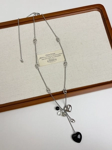 Detail of silver long necklace with black heart bead and metallic pendant on tray