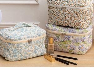 Detailed stack of three quilted cotton makeup bags in various floral prints on a wooden desk