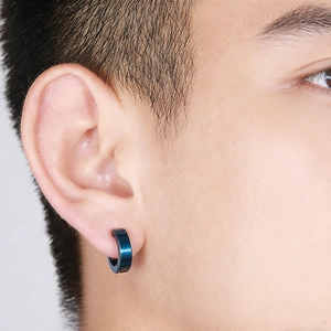 Close-up of a deep blue polished titanium steel huggie earring worn by a model
