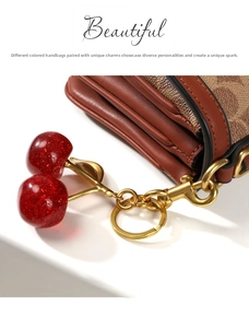 Detail of red resin cherry charm with glitter and gold metal leaf on a brown tote