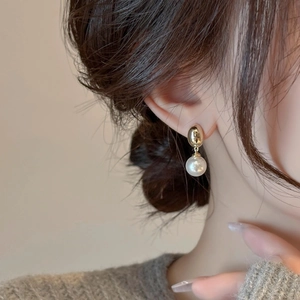 Close-up of a model wearing a vintage pearl drop earring with a polished gold finish