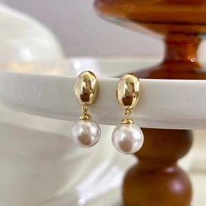 Detailed macro shot of vintage gold-toned oval drop earrings featuring a round white pearl