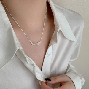 Close-up of dual silver feathers necklace worn on model in a white silk shirt