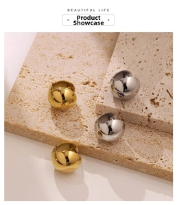 Detailed view of gold and silver hollow sphere hoop earrings on beige textured stone