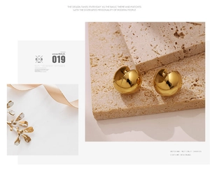 Detail of polished gold hollow sphere stud earrings on elegant textured background