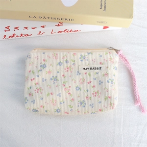Close-up of floral corduroy coin purse with zipper and pink wrist strap on books