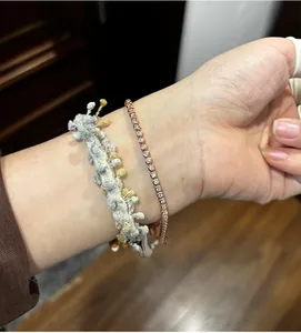 Detail of a rose gold tennis bracelet with moissanite and a woven tassel cord on wrist