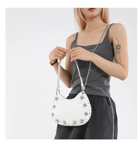 Detailed view of white patent leather crescent bag featuring bold silver rivets and chain strap