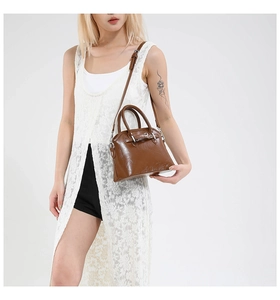 Brown leather handbag with adjustable strap shown on a model in a white studio
