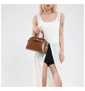 Detail of a brown glossy patent leather shell handbag with decorative buckles and handles